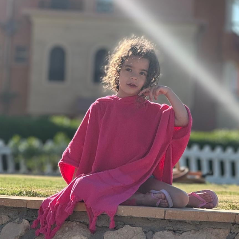 A child standing on a beach wearing a poncho.