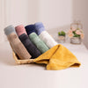 A collection of folded face towels in various colors including beige, blue, pink, gray, and yellow, displayed in a brown basket.