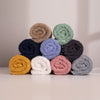 A stack of folded hand towels in various solid colors including beige, blue, green, yellow, pink, and gray, arranged on a light surface.